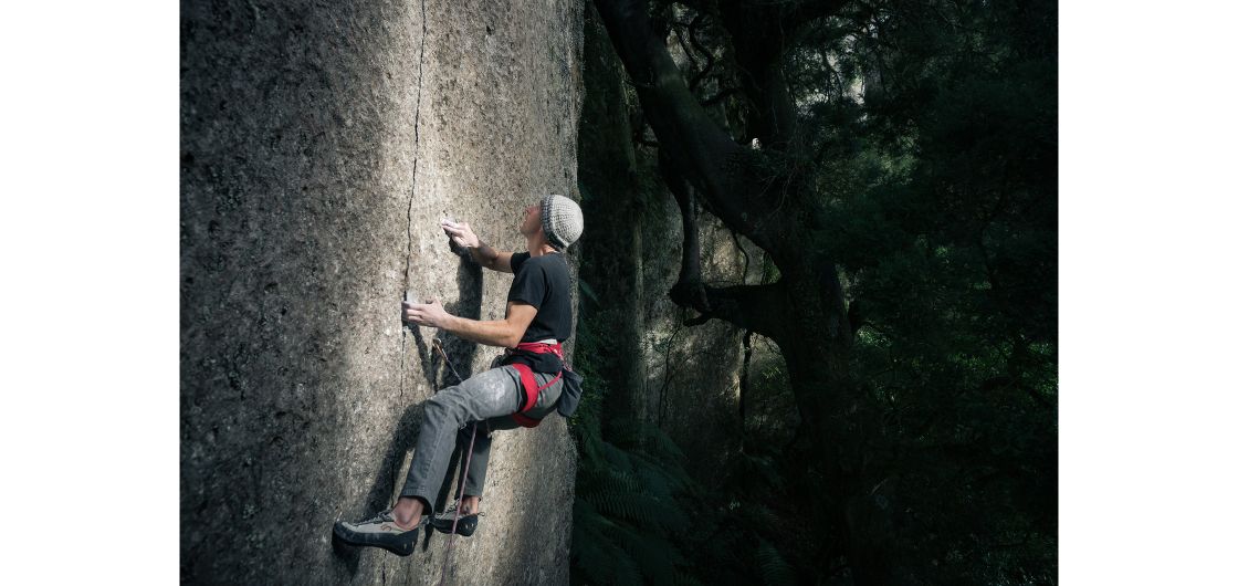 Climber on sheer wall in dark forest