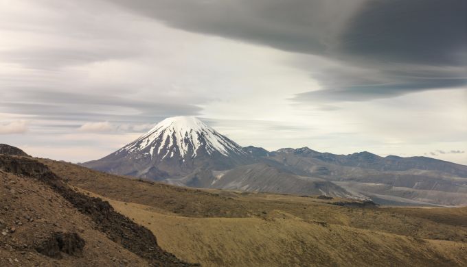 A snow-capped conical volcano with cloud formations
