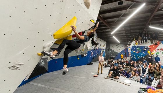 Female climbing in competition with crowd watching.