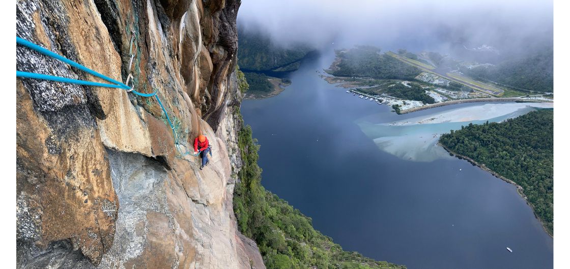 Climber on orange granite above fiord.