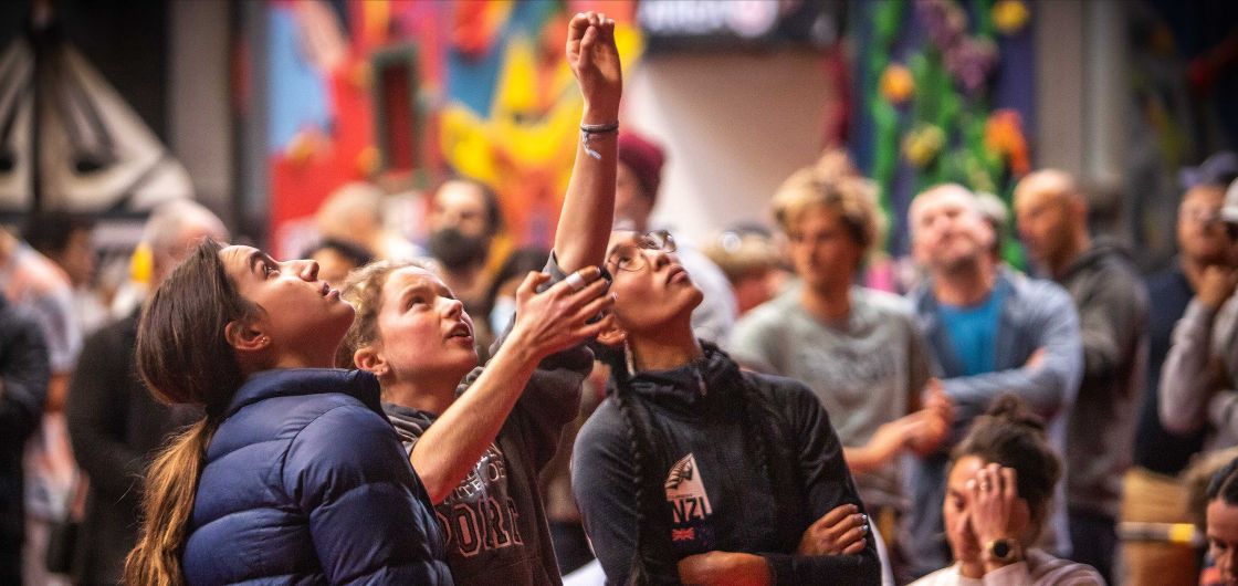 Open Women's Finalists preview the route. Photo: Judah Plester Competition climbers observe a route from the ground, miming sequences.