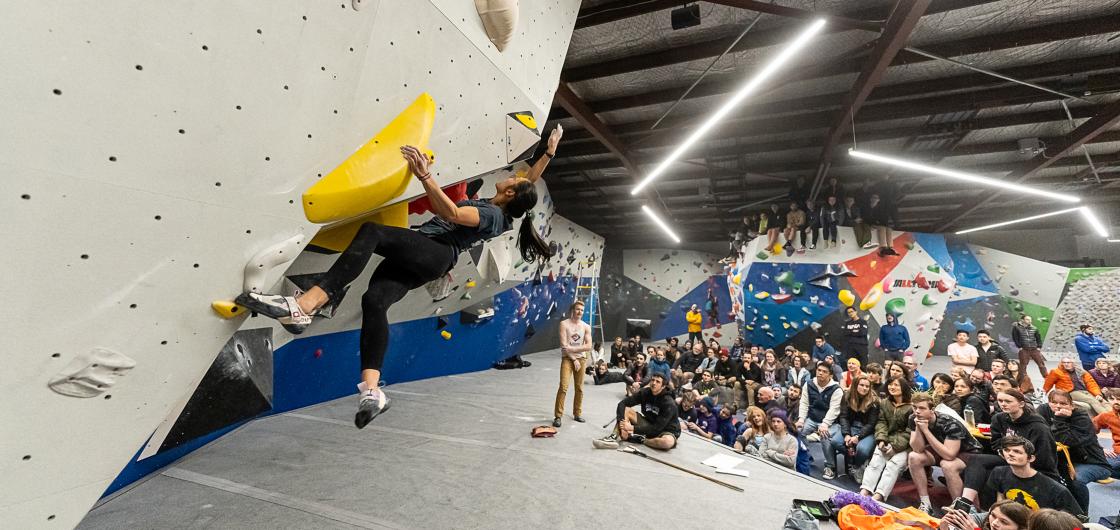 Female climbing in competition with crowd watching.