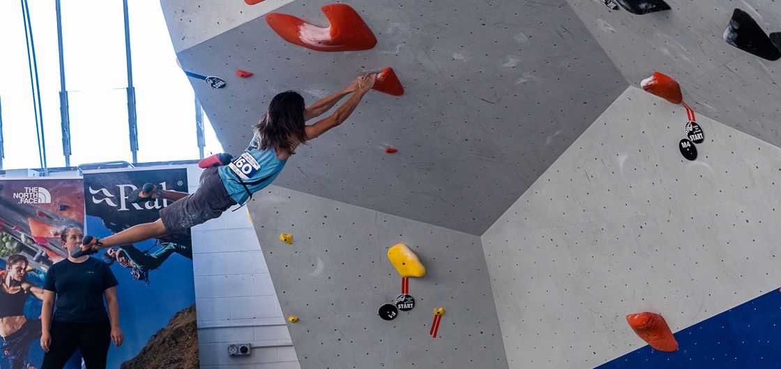 Climber moves dynamically on competition boulder wall