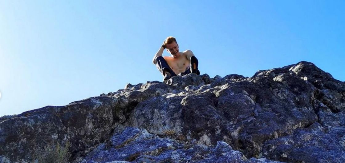 Man smiles happily on top of rock.