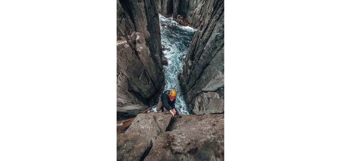 Rowan Bulpit pulling the final moves of pitch 1 of Deep Play on the Totem Pole, Tasmania. Photo: Adam Flower. Rock climber above sea