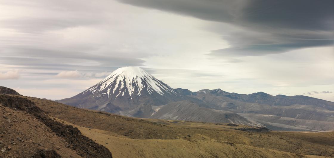 A snow-capped conical volcano with cloud formations