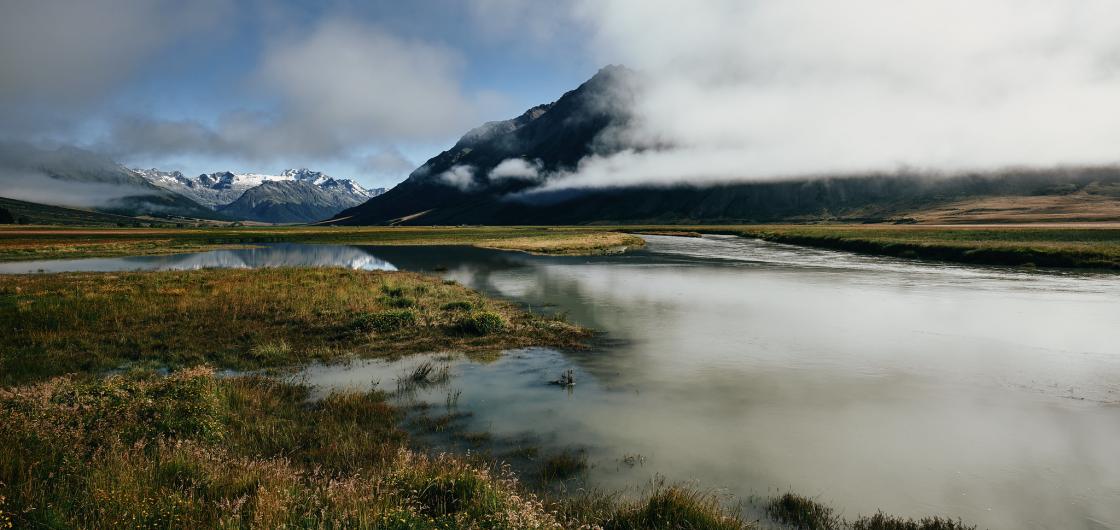 Ahuriri Valley A valley view with distant mountains and low cloud reflected in a small lagoon.