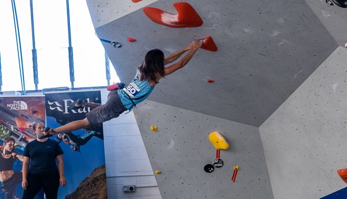 Climber moves dynamically on competition boulder wall