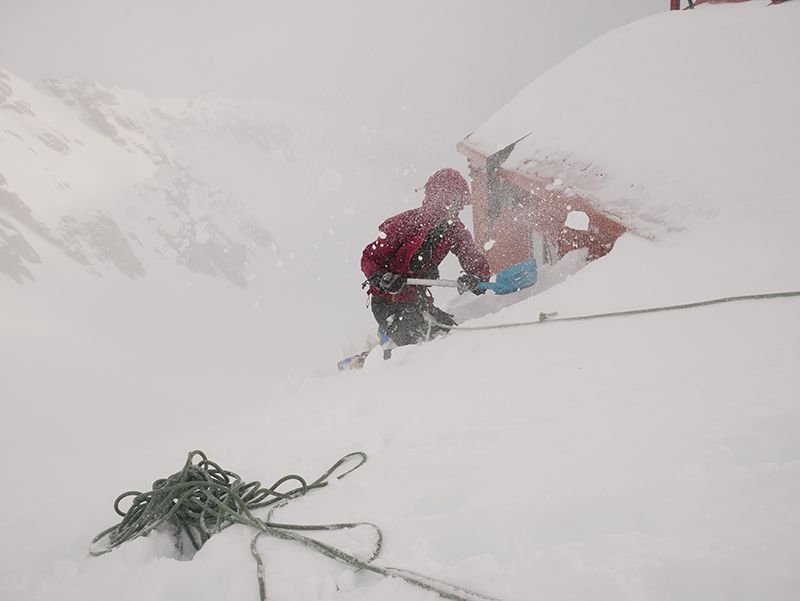 Climber digging out hut in blizzard